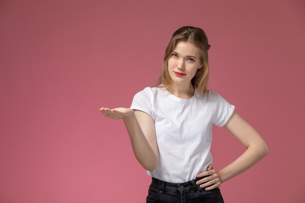 Front view young attractive female in white t-shirt posing with raised hand on pink wall model female pose color female young