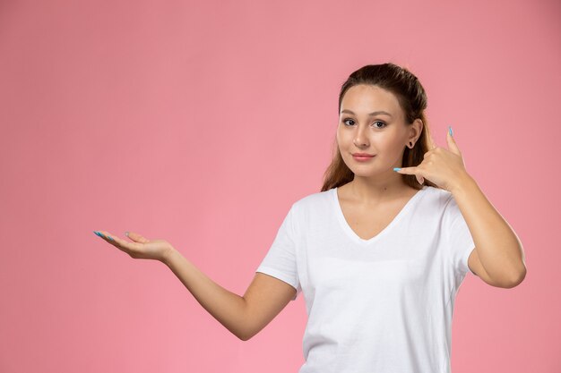 Front view young attractive female in white t-shirt posing with slight smile on pink background