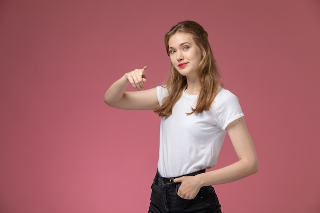 Front view young attractive female in white t-shirt posing with slight smile on pink wall model color female young