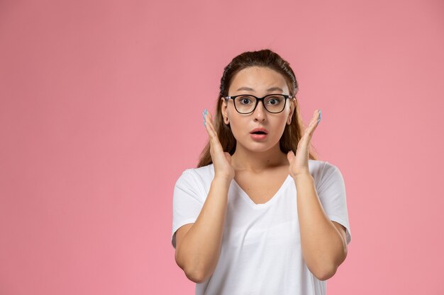 Front view young attractive female in white t-shirt posing with surprised expression on the pink background