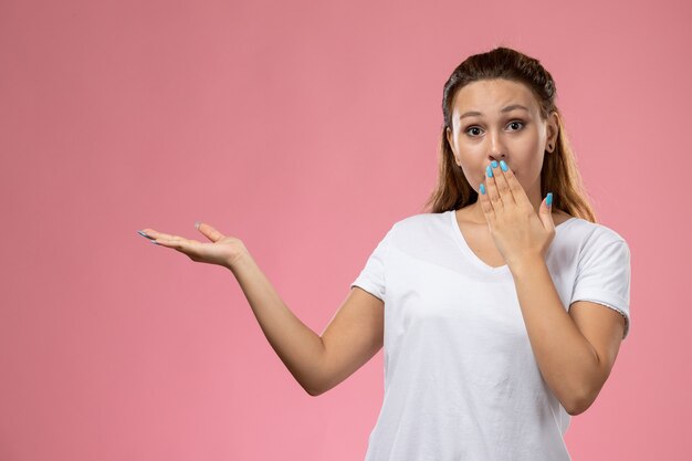 ピンクの背景に驚きの表情でポーズをとって白いtシャツで正面の若い魅力的な女性