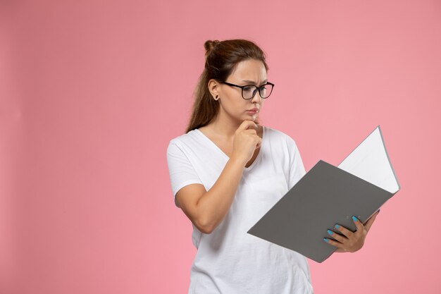 ピンクの背景に灰色のedファイルを読んで白いtシャツで正面の若い魅力的な女性