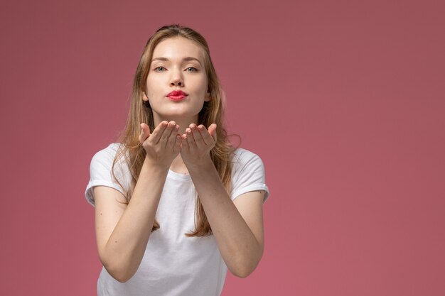 濃いピンクの壁のモデルカラーの女性の若い女の子にエアキスを送信する白いTシャツの正面図若い魅力的な女性