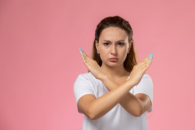Front view young attractive female in white t-shirt showing ban sign with displeased expression on the pink background