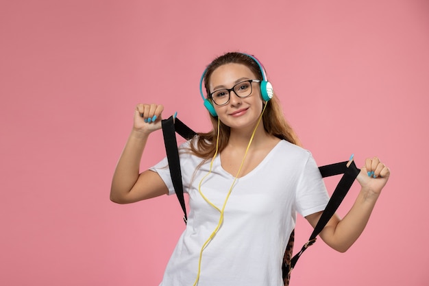 Front view young attractive female in white t-shirt smi and listening to music on the pink background