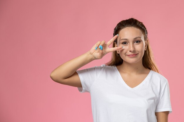 ピンクの背景にポーズをとって白いtシャツsmiで正面の若い魅力的な女性