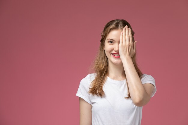 웃 고 분홍색 벽 모델 색상 여성 젊은에 그녀의 얼굴의 절반을 덮고 흰색 티셔츠에 전면보기 젊은 매력적인 여성
