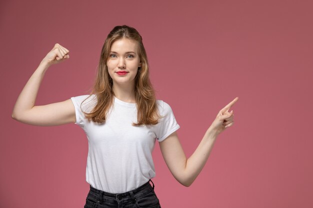 Front view young attractive female in white t-shirt smiling and flexing on the dark-pink wall model color female young girl