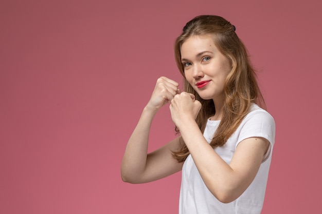 Front view young attractive female in white t-shirt smiling and posing on pink desk model color female young girl