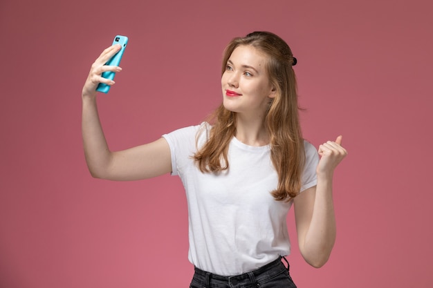Front view young attractive female in white t-shirt taking a selfie with smile on pink wall model color female young