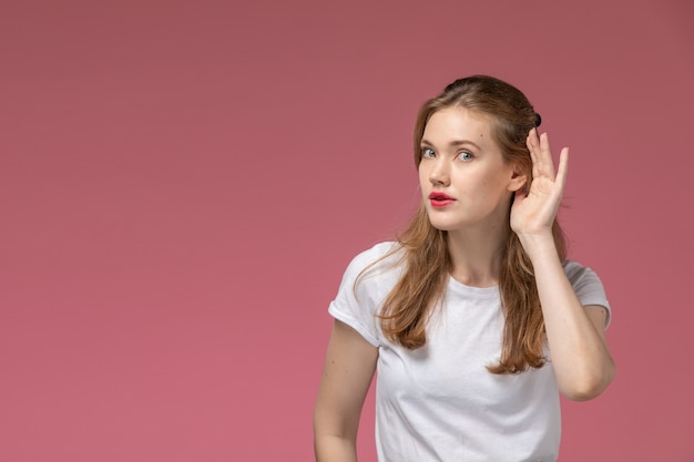 Front view young attractive female in white t-shirt trying to hear out on the pink wall model female pose color photo