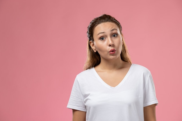 ピンクの背景に何かを伝えようとしている白いtシャツで正面の若い魅力的な女性