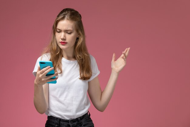ピンクの壁のモデルの色の若い女性の彼女の電話を使用して白いTシャツの正面図若い魅力的な女性