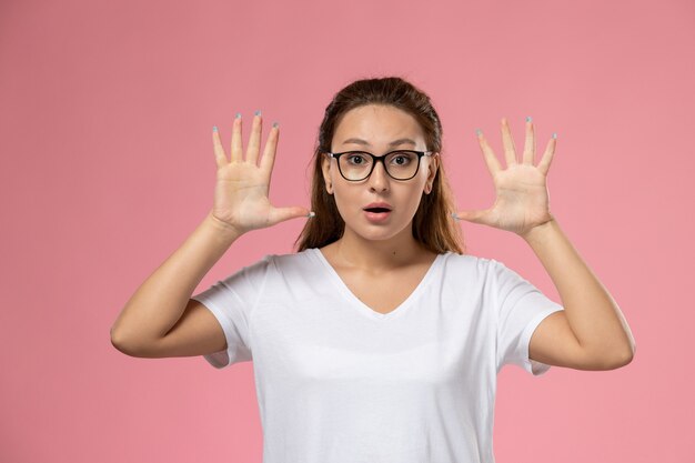 ピンクの背景に驚いた表情で白いtシャツの正面の若い魅力的な女性