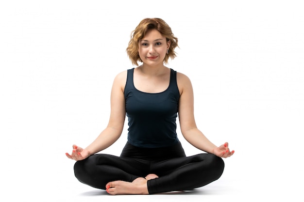 Free photo a front view young attractive girl in blue shirt and black trousers sport outfit doing workouts gymnastics meditating on the white