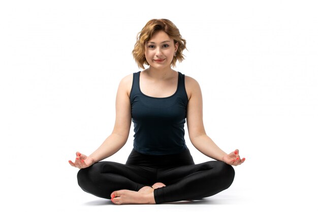 A front view young attractive girl in blue shirt and black trousers sport outfit doing workouts gymnastics meditating on the white