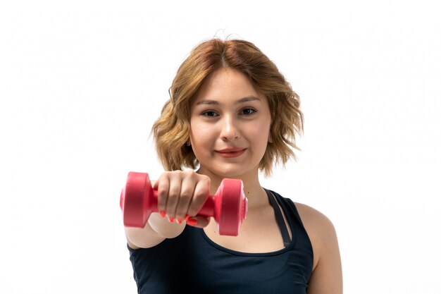 A front view young attractive girl in blue shirt and black trousers sport outfit doing workouts with dumbbells on the white