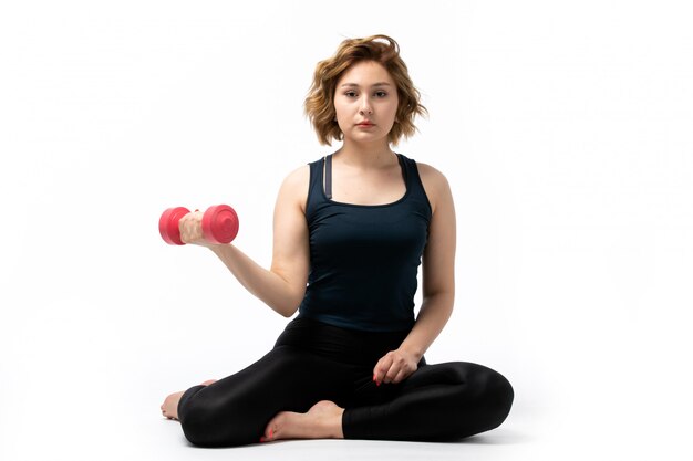 A front view young attractive girl in blue shirt and black trousers sport outfit doing workouts with dumbells on the white