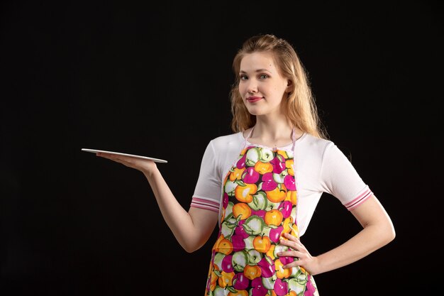 A front view young attractive girl in colorful cape holding paints smiling on the black background cleaning housewife