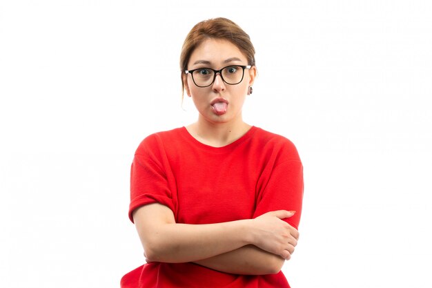 A front view young attractive girl in red t-shirt wearing black jeans in sunglasses making funny faces on the white