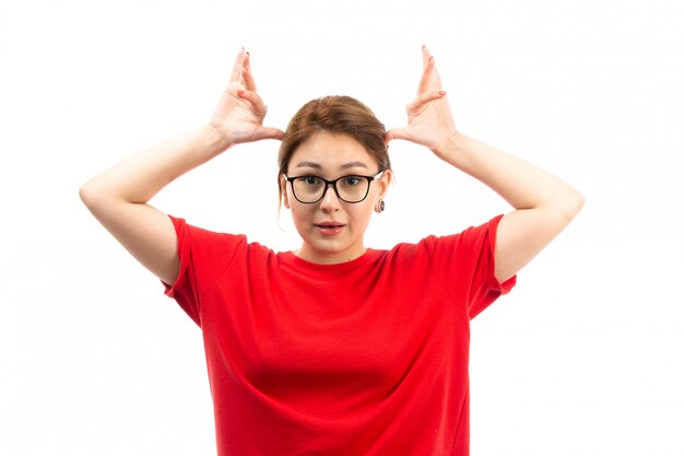 A front view young attractive girl in red t-shirt wearing black jeans in sunglasses posing on the white