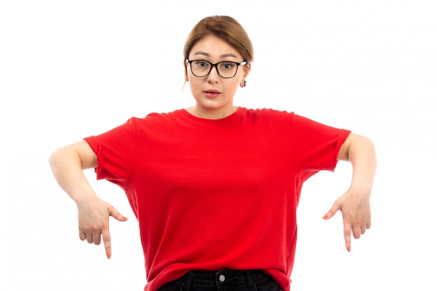 A front view young attractive girl in red t-shirt wearing black jeans in sunglasses posing on the white