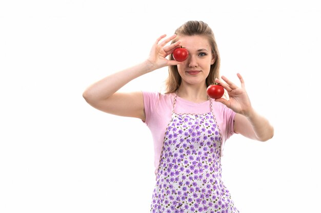 A front view young attractive housewife in pink shirt colorful cape holding red tomatoes posing on the white background cuisine kitchen female