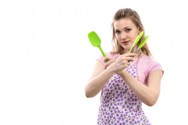 白い背景の料理キッチン女性にプラスチックキッチン家電を保持しているピンクのシャツカラフルなケープのポーズで正面の若い魅力的な主婦