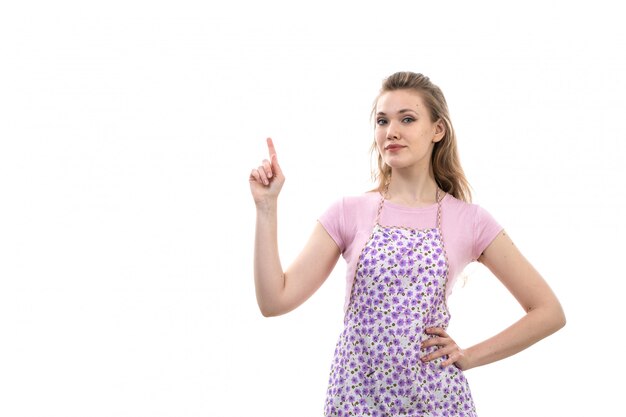 A front view young attractive housewife in pink shirt colorful cape posing on the white background cuisine kitchen female