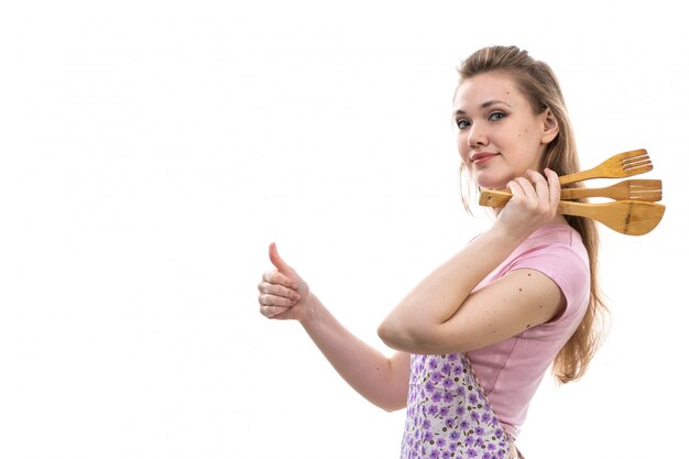 A front view young attractive housewife in pink shirt colorful cape smiling posing holding wooden appliances on the white background cuisine kitchen female