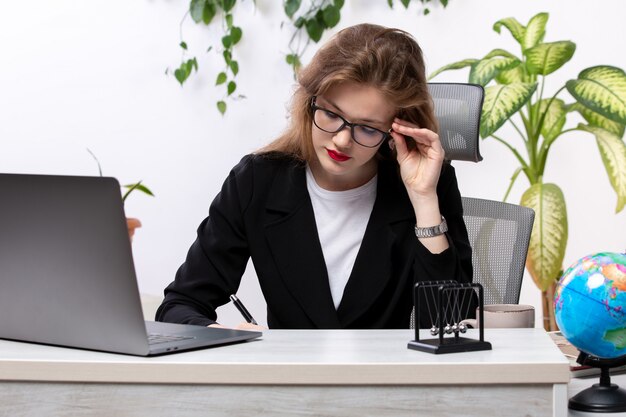 A front view young attractive lady in black jacket and white shirt in front of table working with laptop work business technologies