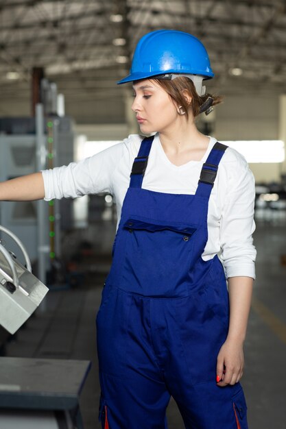 A front view young attractive lady in blue construction suit and helmet controlling machines in hangar working in the area buildings architecture construction