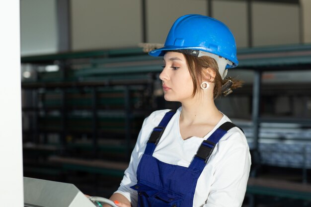 青い建物の正面の若い魅力的な女性と日中の建物の建築工事中に働く格納庫のヘルメット制御機