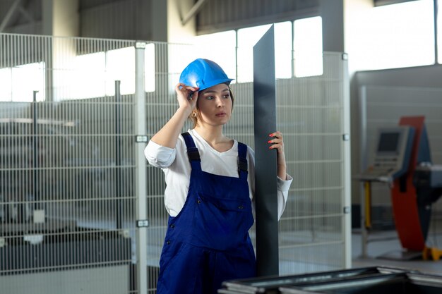 A front view young attractive lady in blue construction suit and helmet working holding heavy metallic detail during daytime buildings architecture construction