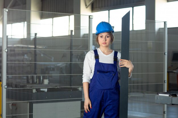 A front view young attractive lady in blue construction suit and helmet working holding heavy metallic detail during daytime buildings architecture construction