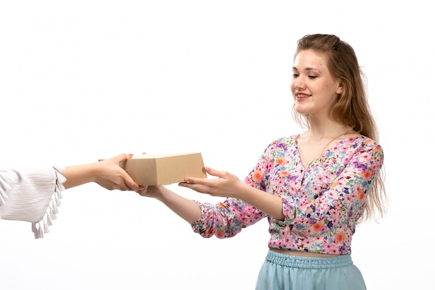 A front view young attractive lady in colorful flower designed shirt and blue skirt getting little package on the white