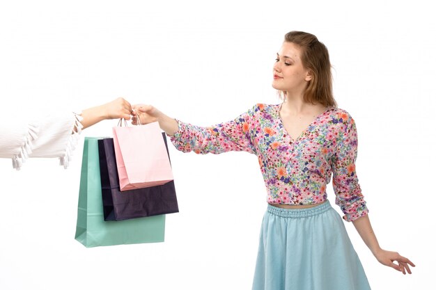 화려한 꽃 디자인 셔츠와 파란색 치마에 전면보기 젊은 매력적인 여자는 흰색에 쇼핑 패키지를 받고