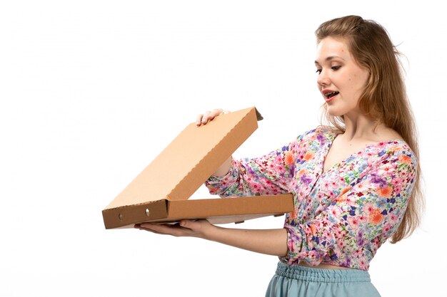 A front view young attractive lady in colorful flower designed shirt and blue skirt holding brown box opening it on the white