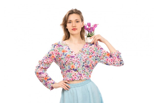 カラフルな花の正面の若い魅力的な女性がシャツと白に紫の花の植物を保持している青いスカートをデザイン