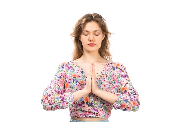 A front view young attractive lady in colorful flower designed shirt and blue skirt posing praying on the white