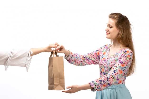 A front view young attractive lady in colorful flower designed shirt and blue skirt taking brown package smiling on the white