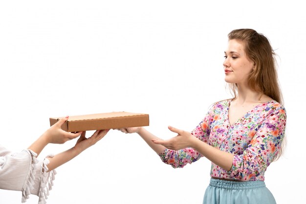 A front view young attractive lady in colorful flower designed shirt and blue skirt taking brown package on the white