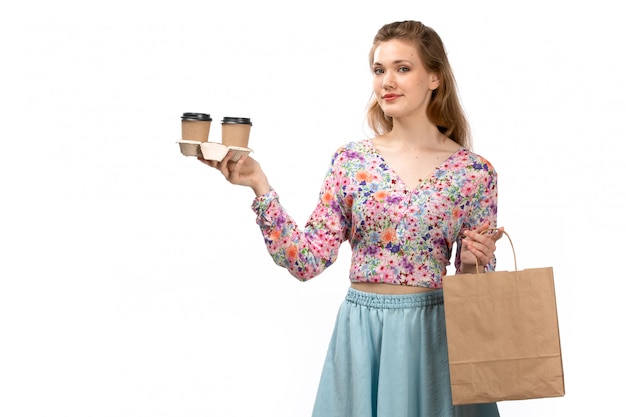 A front view young attractive lady in colorful shirt and blue skirt holding brown package with coffee on the white