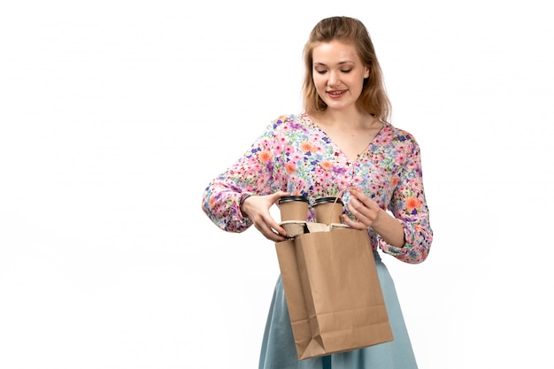 A front view young attractive lady in colorful shirt and blue skirt holding brown package with coffee on the white