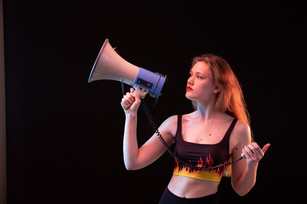 Free photo a front view young attractive lady in fire shirt and black trousers using megaphone on the black background volume loud