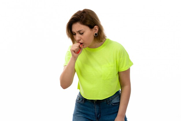 A front view young attractive lady in green shirt and blue jeans coughing on the white