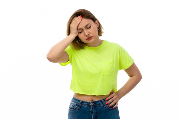 A front view young attractive lady in green shirt and blue jeans suffering from headache on the white