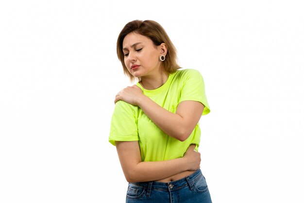 A front view young attractive lady in green shirt and blue jeans suffering from shoulder ache on the white