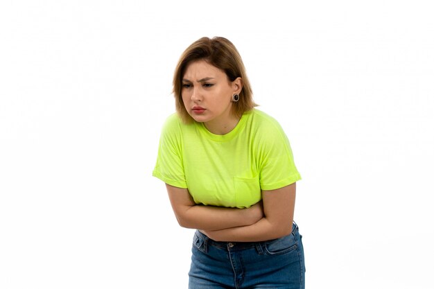 A front view young attractive lady in green shirt and blue jeans suffering from stomachache on the white