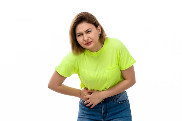 A front view young attractive lady in green shirt and blue jeans suffering from stomachache on the white